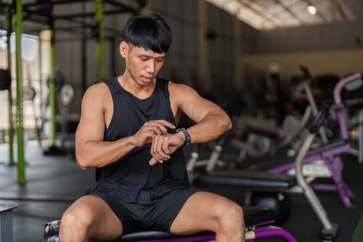 A young man in a gym checking his smartwatch for workout metrics, highlighting the integration of fitness and technology.