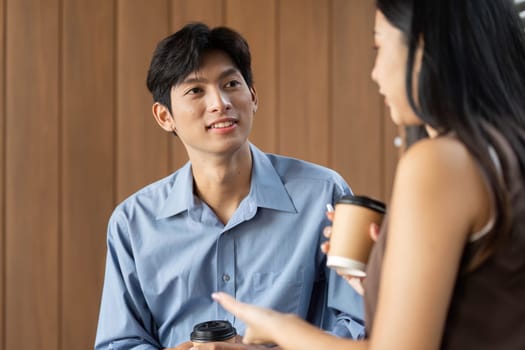 A young businessman and woman engaging in a lively conversation with coffee cups in a stylish office setting, showcasing collaboration and teamwork.