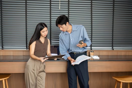 A businesswoman and businessman examining reports and digital content, engaged in a productive meeting in a contemporary workspace.