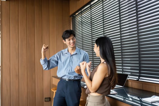 Two young professionals share a joyful moment, celebrating their achievements and fostering a positive team spirit in a stylish workspace.