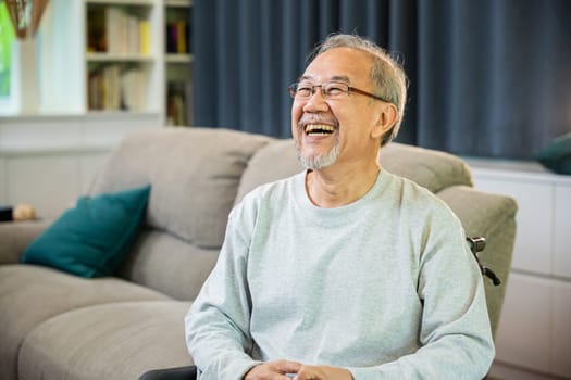 Portrait Asian old man alone relaxing on comfortable couch in cozy living room at home, happy smiling positive older senior male laughing at funny joke and thinking about good future