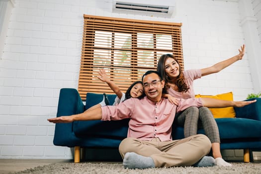 An interracial family shares a moment of joy and togetherness at home. Playing plane games a father with his daughter on his shoulders and a smiling mother showcase the essence of a supportive family.