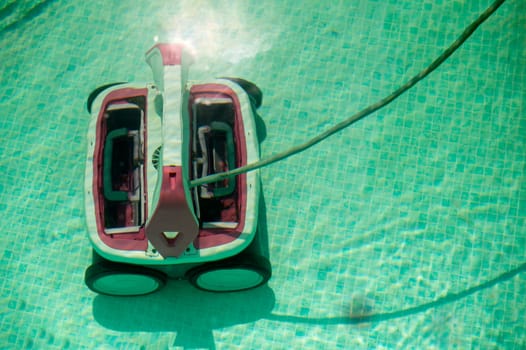 Automatic robotic pool vacuum cleaner under water cleaning the floor. Water robot vacuum cleaner cleans, removes debris on the bottom, walls of the pool, top view through translucent water.