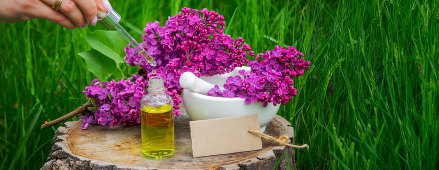 Lilac essential oil on a wooden stump. Bottle with aromatic oil and lilac flowers.