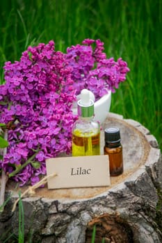 Lilac essential oil on a wooden stump. Bottle with aromatic oil and lilac flowers.