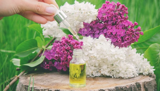 Lilac essential oil on a wooden stump. Bottle with aromatic oil and lilac flowers.