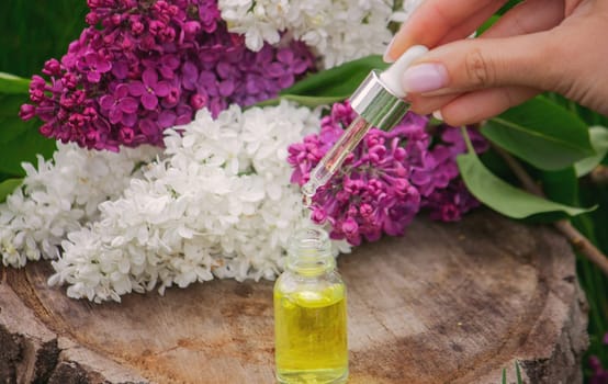 Lilac essential oil on a wooden stump. Bottle with aromatic oil and lilac flowers.