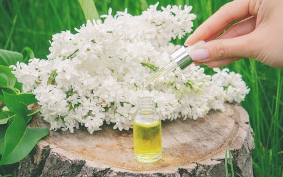 Lilac essential oil on a wooden stump. Bottle with aromatic oil and lilac flowers.