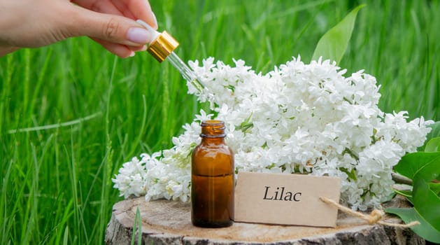 Lilac essential oil on a wooden stump. Bottle with aromatic oil and lilac flowers.