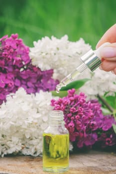 Lilac essential oil on a wooden stump. Bottle with aromatic oil and lilac flowers.