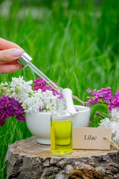 Lilac essential oil on a wooden stump. Bottle with aromatic oil and lilac flowers.
