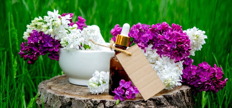 Lilac essential oil on a wooden stump. Bottle with aromatic oil and lilac flowers.
