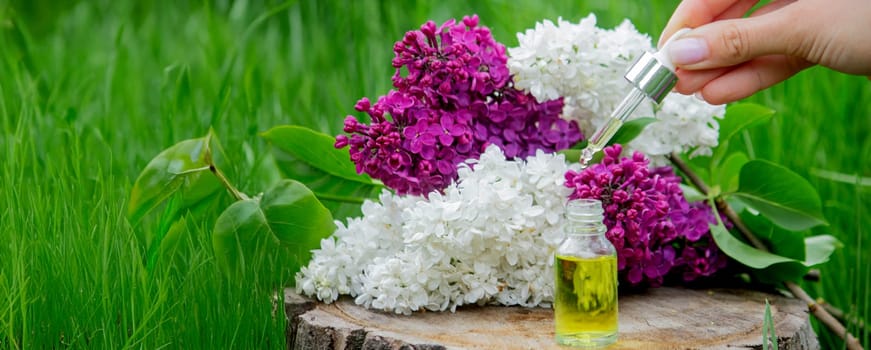 Lilac essential oil on a wooden stump. Bottle with aromatic oil and lilac flowers.