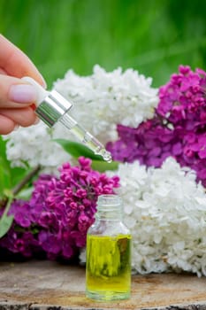 Lilac essential oil on a wooden stump. Bottle with aromatic oil and lilac flowers.
