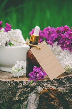 Lilac essential oil on a wooden stump. Bottle with aromatic oil and lilac flowers.