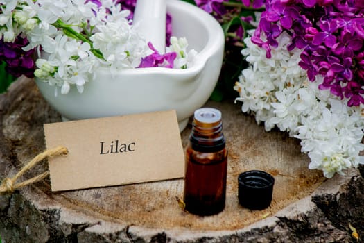 Lilac essential oil on a wooden stump. Bottle with aromatic oil and lilac flowers.