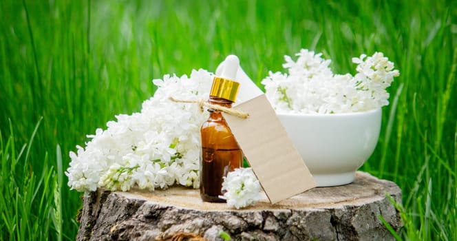 Lilac essential oil on a wooden stump. Bottle with aromatic oil and lilac flowers.