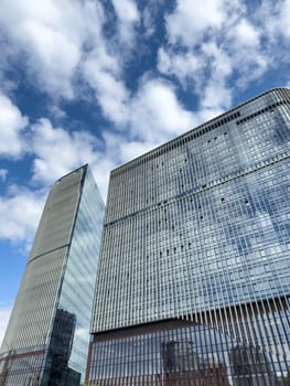 Wide angle view of modern business skyscrapers with mirrored glass and metal grid design. Bright sky with clouds reflects ambition, growth and futuristic corporate architecture