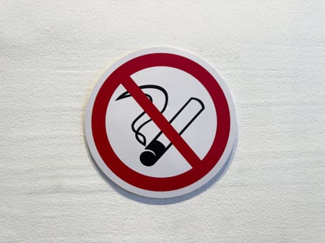 Close up of no smoking sign on white wall. Red circle with cigarette symbol and diagonal line emphasizes public health, safety and clean air in indoor environments