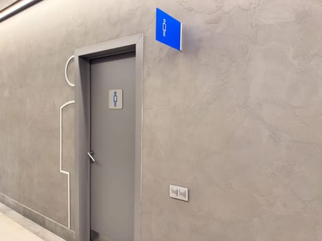 Modern men restroom door with minimalist signage in public interior. Gray textured wall, sleek design, and clear blue icon make it easy to navigate commercial or retail spaces