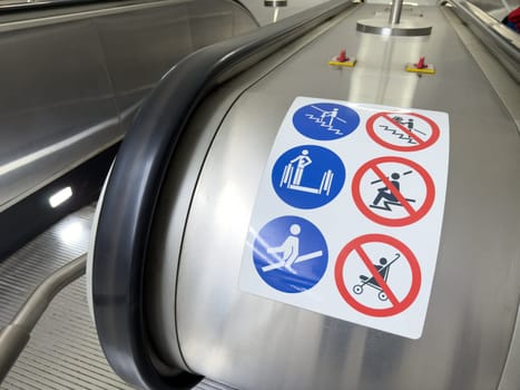 Modern escalator with detailed pictogram safety instructions on metallic surface. Focus on universal visual language for public space navigation and risk prevention