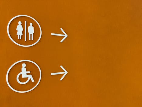 Modern restroom direction sign with male, female and wheelchair symbols on bold orange wall, pointing to the right. Accessible and inclusive design for public facilities navigation