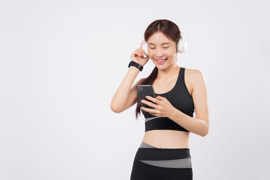 Holding her phone while browsing application music on the phone, this athletic Asian woman in sportswear listens with joy through her headphones during a workout. isolated studio white background