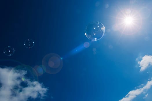 Soap bubbles in the blue sky with isolated clouds backlit by the sun.