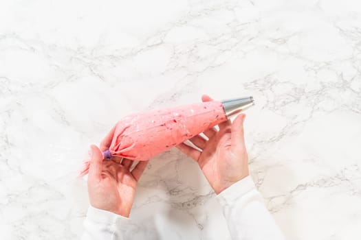 A piping bag filled with vibrant cranberry buttercream, ready for decorating lemon spritz cookies. The smooth buttercream is prepared for precise and beautiful decoration with a star tip nozzle.