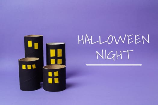 Cardboard house with a sign that says Halloween Night. The sign is on a purple background. The houses are made of cardboard and are arranged in a row