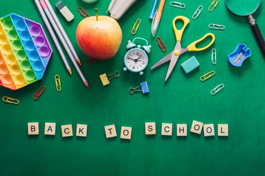 Green background with a word that says back to school. There are also some other items on the background such as a clock, scissors, and a pencil