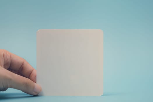 Female hand holding blank white note against blue background. Concept of message, communication, announcement, copy space, and marketing or personal note.