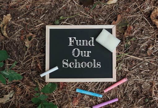 Chalkboard with the words fund Our Schools written on it. There are also some crayons on the ground