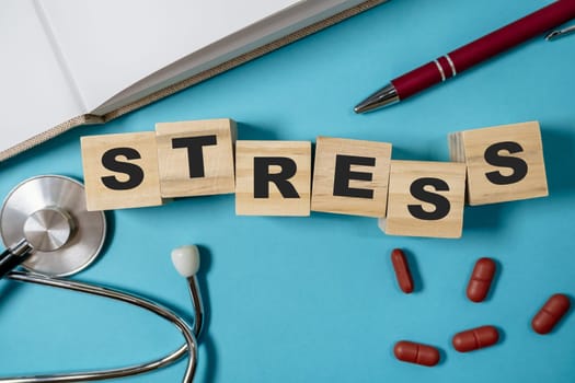 Stack of wooden blocks with the word stress written on them. The blocks are arranged in a way that they spell out the word, and there are also some pills on the table