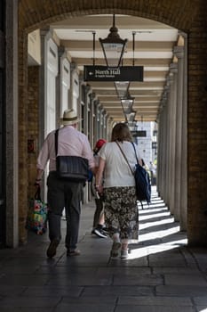 London, UK - May 13, 2025 - Vertical view of An elderly couple holding hands walking through the symmetrical arches and old fashioned street lamps hang from the ceiling at Covent Garden in London, Romantic and elderly healthy lifestyle concept, use it as your Wallpaper, Poster and Space for text, Selective focus.