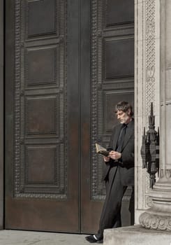 London, UK - May 13, 2025 - A man in suit standing in a doorway leaning against the door frame, reading a Haruki Murakami book. use it as your Wallpaper, Poster and Space for text, Selective focus.