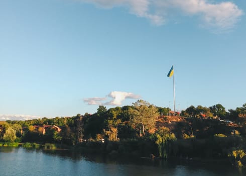 Flagpole is standing in the middle of a field. The flag is blue and yellow. The sky is clear and blue