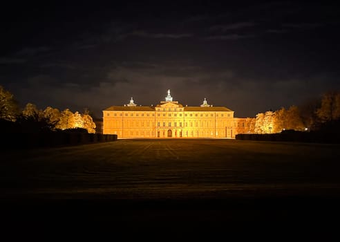Large building with a clock tower is lit up at night. The building is surrounded by a grassy field