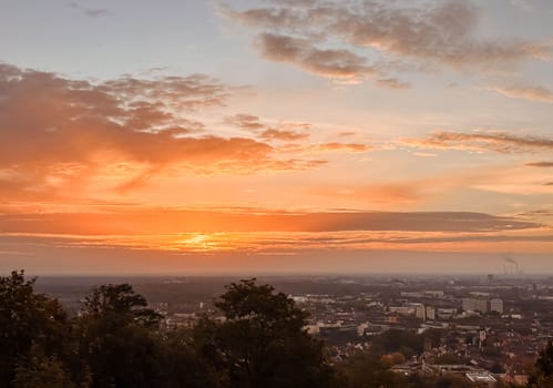 The sun is setting over a city with a beautiful orange sky. The sky is filled with clouds and the sun is setting behind them