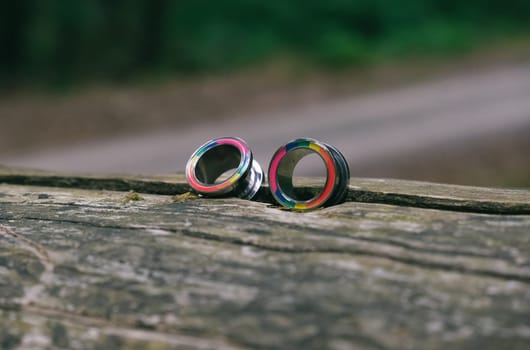 Two colorful earrings are sitting on a wooden surface. The earrings are multi-colored and have a unique design