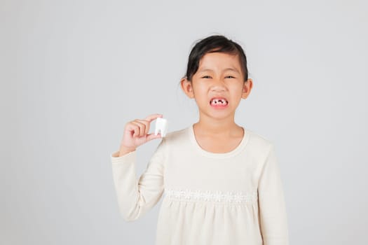 Kid girl smiles with missing tooth, holding model in hand for dentist talk. Showing teeth gap to explain dental care, child development, and natural tooth loss. isolated white background