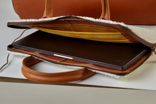 Brown leather laptop sleeve with soft inner lining protecting an ultrabook, placed on a white table