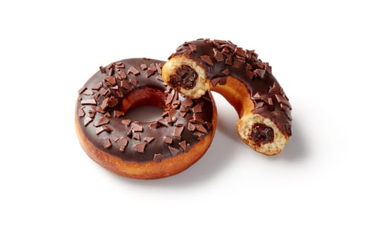 Two delicious chocolate donuts, one whole and one half, filled with chocolate cream and covered with chocolate chips, isolated on white