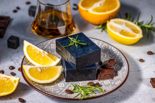 Gourmet black cheese served with lemon slices, rosemary sprigs, chocolate pieces, and a glass of whiskey with ice