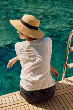 A girl in a hat sits on the edge of a sailing boat and enjoys the views and azure color of the sea on a sunny day. High quality photo