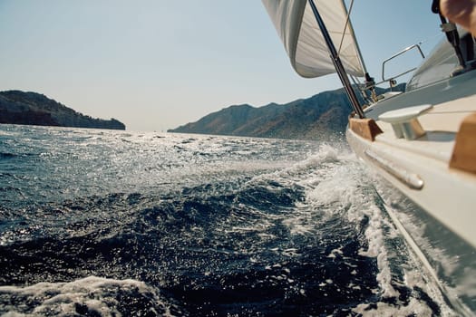 waves crash against the side of a sailing boat traveling at speed, splashes glow in the sun, burning in the background, the glare of the sun on the water. High quality photo