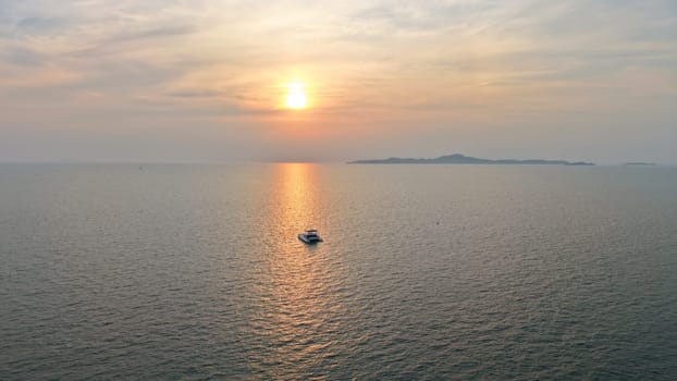 Golden sun setting over a tranquil ocean, casting a warm glow on the water as a catamaran sails peacefully towards the horizon, with a distant island adding to the serene seascape