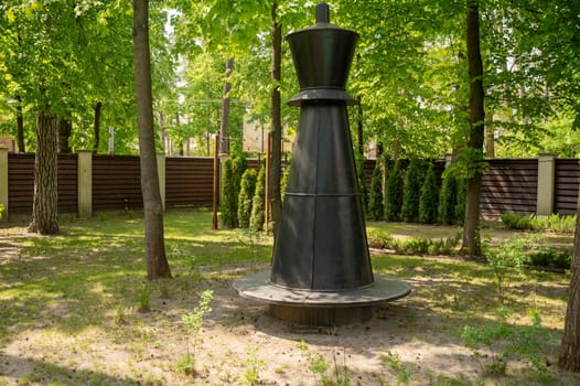 Bench in the park in the form of a chess piece in the park. Park with tall trees, green lawn on a sunny day