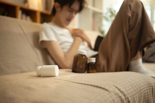 Sick man suffering at home with medicine bottles.