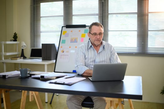 Confident older adult using laptop and managing tasks in modern workspace.